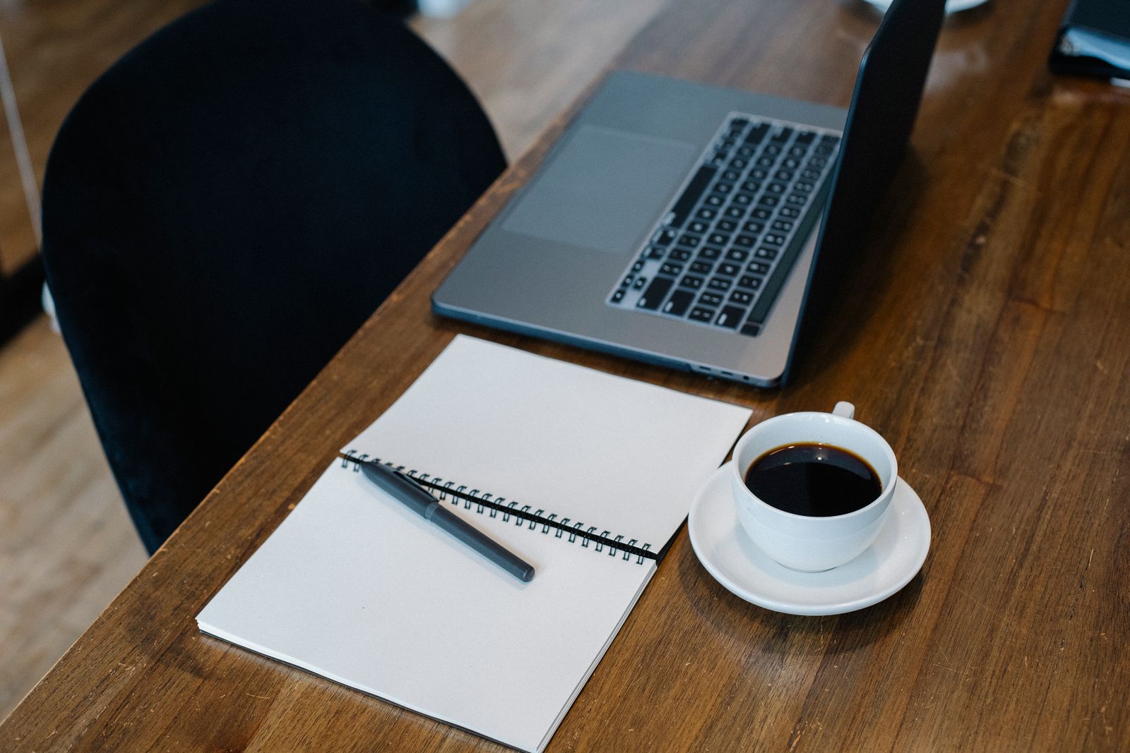 A laptop, open notebook, and cup of coffee on a wooden desk