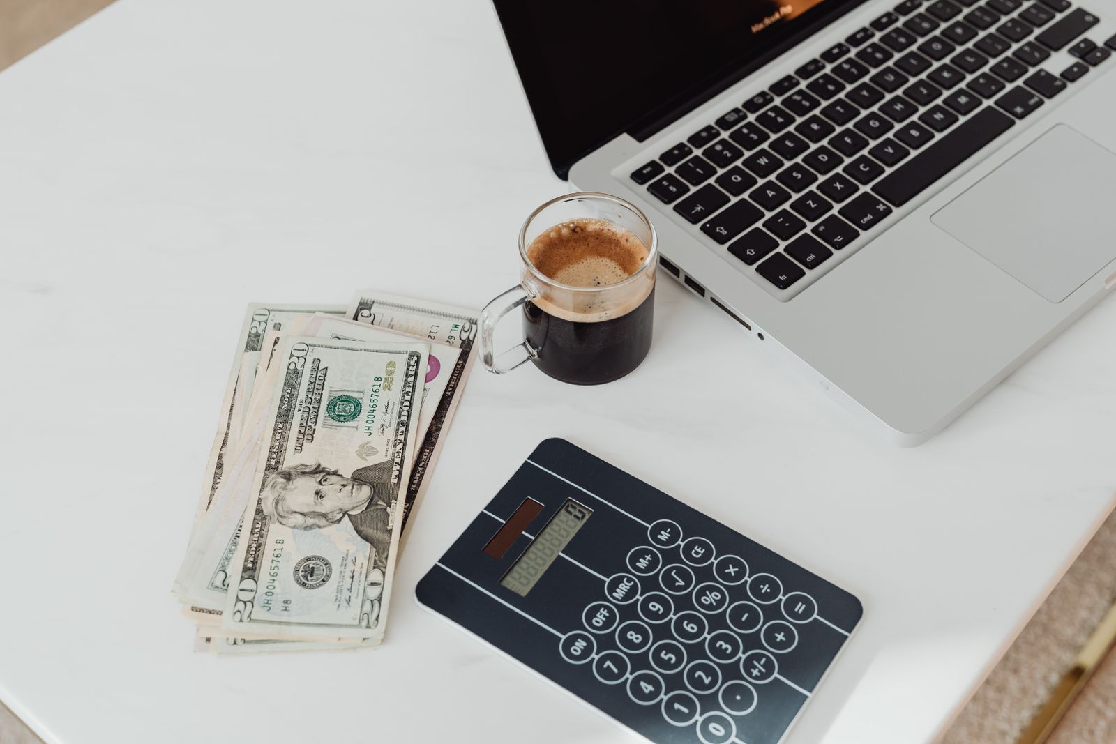 A calculator, cash, and a laptop on a white desk