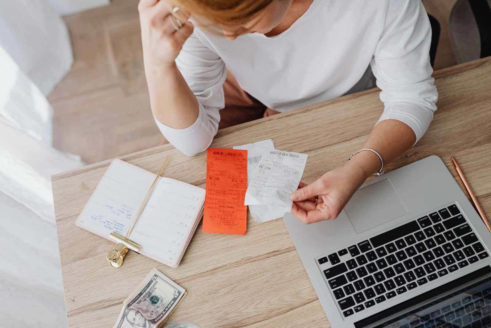 A person reviewing paper invoices and receipts next to an open laptop