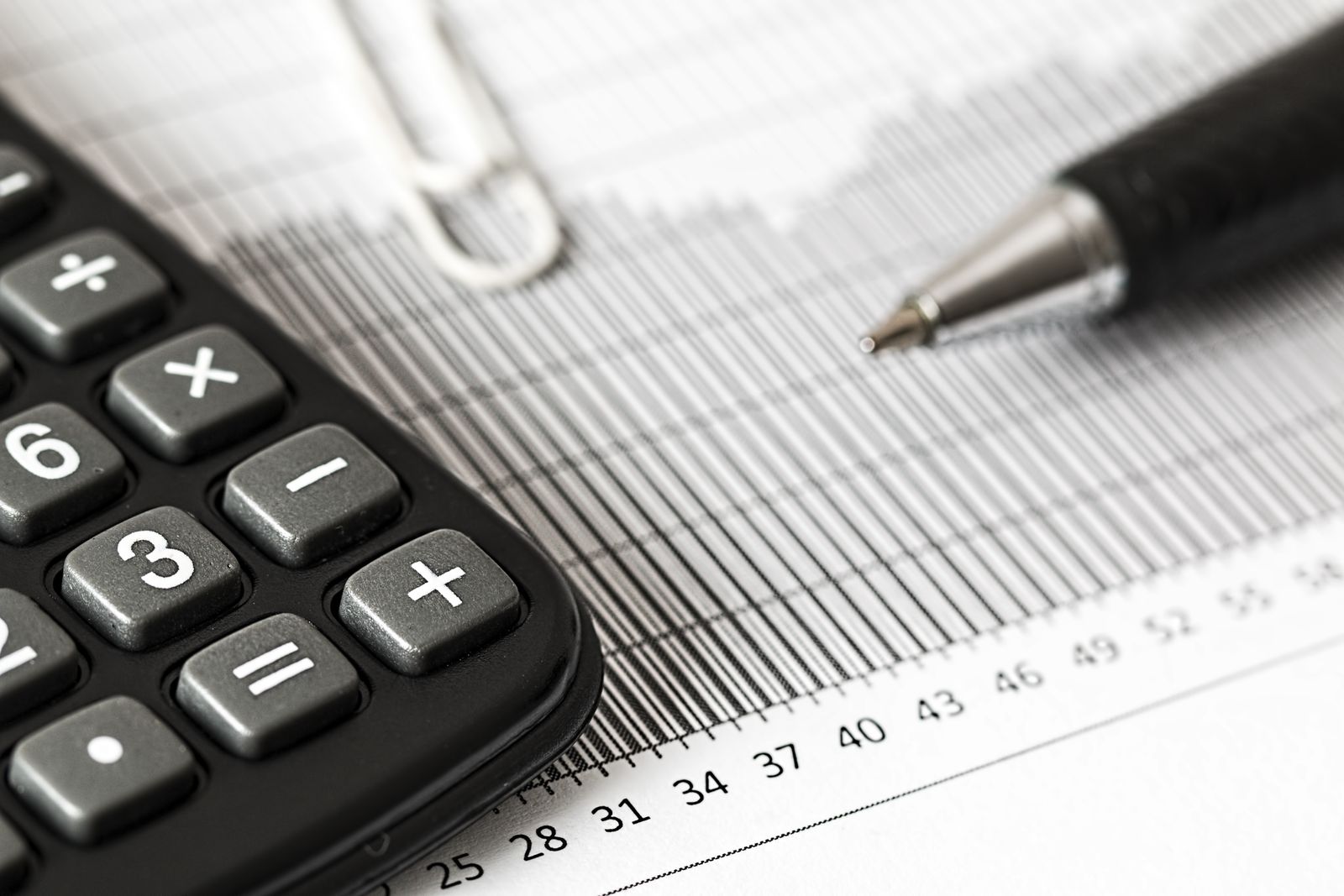 A checklist and calculator on a desk next to an open laptop showing spreadsheets
