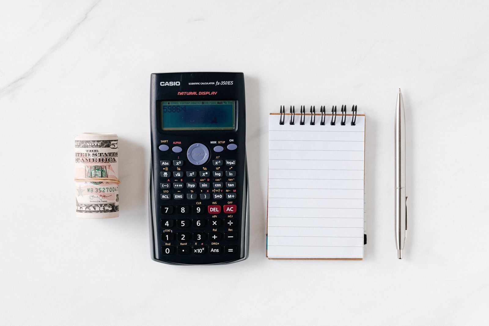 A calculator, rolled cash, and a notepad on a desk
