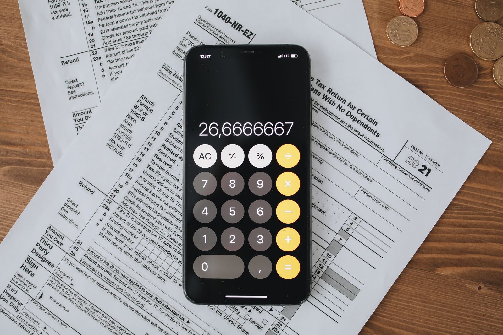 A phone calculator resting on printed federal tax forms next to loose coins