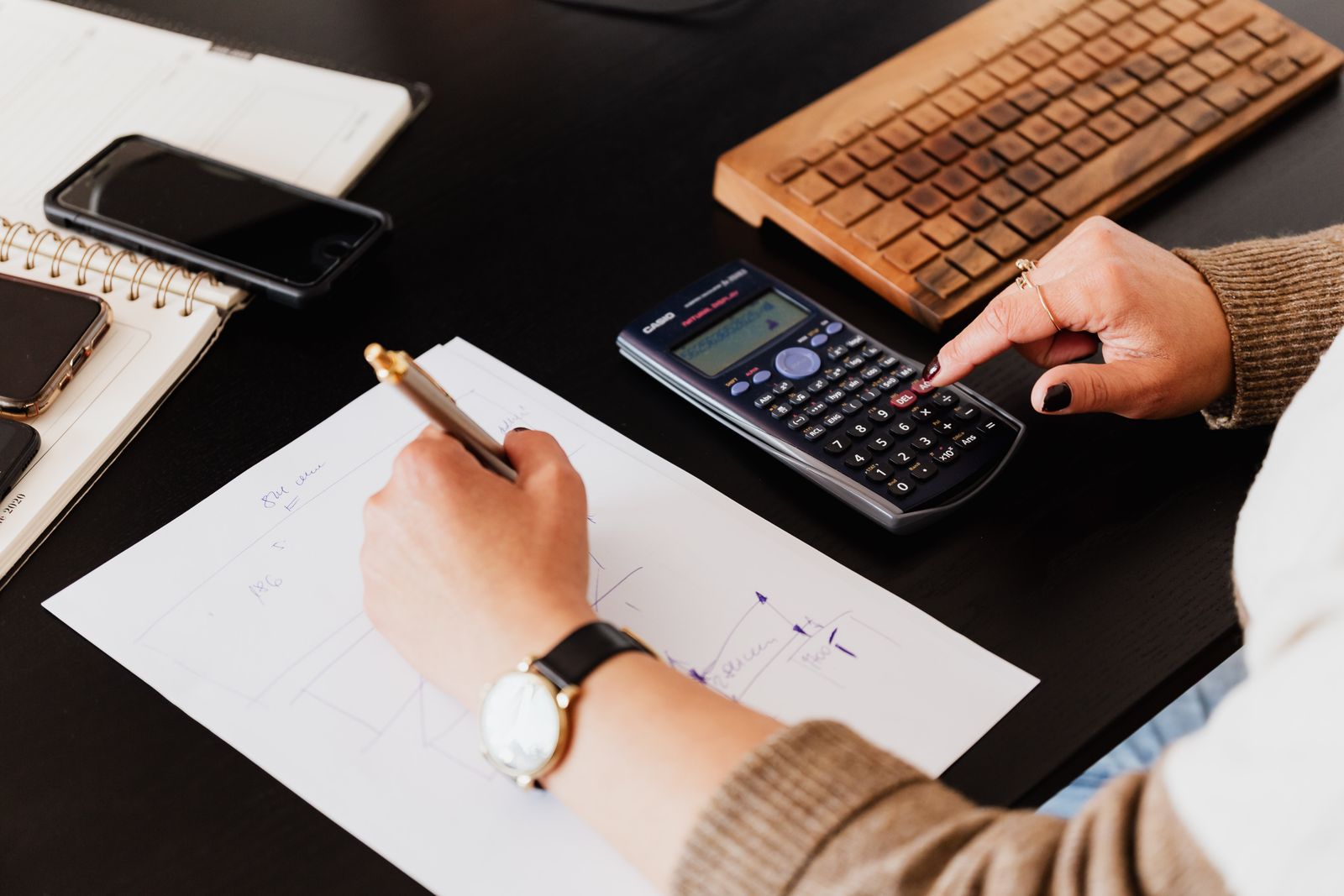 A bookkeeper checking figures on a calculator while writing on paper